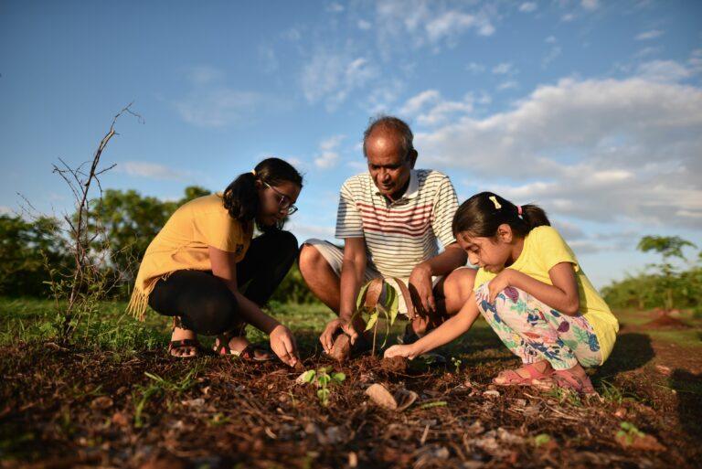 image extracted from Booking.com Sustainable Travel Report: two little girls plant a plant with an elderly man