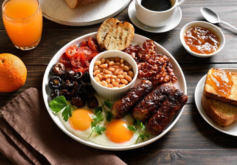 English breakfast served in a rental property with fried eggs, bacon, sausage, beans, tomatos and mushrooms on wooden table. 