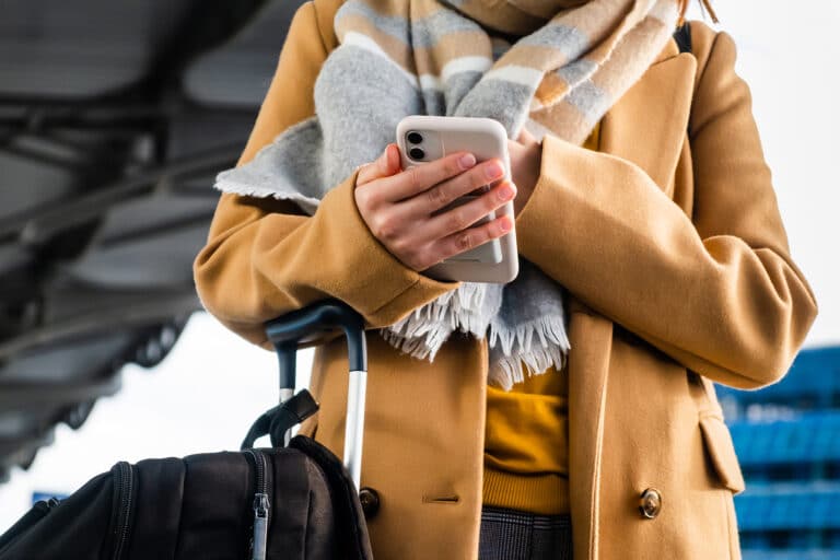 donna con giacca gialla compila il check-in online sullo smartphone mentre si trova alla stazione dei treni