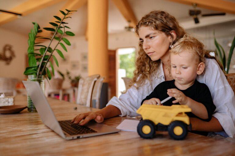 a woman manages her vacation rental on her laptop while taking care of her kid